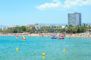 A beach with clear blue water, palm trees, and a tall building in the background. - Apartment in Salou, 2 minutes from the beach (Salou)