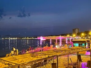 A beachside area with tents and chairs, a water body, and a distant city skyline. - Apartment in Salou, 2 minutes from the beach (Salou)