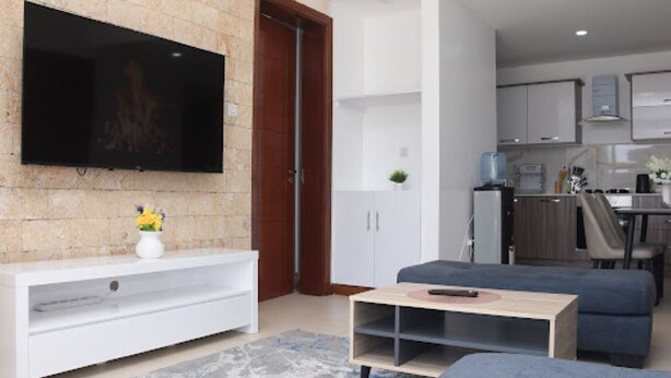 A modern living room with a flat-screen TV, a white entertainment unit, a blue sofa, and a coffee table. - Imagine Luxury- 2 Bedroom (Nairobi)