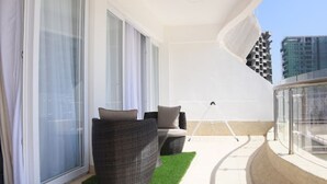 A balcony with a wicker sofa, a small table, and a glass railing. - Imagine Luxury- 2 Bedroom (Nairobi)