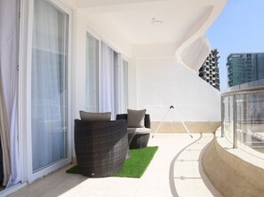 A balcony with a wicker sofa, a small table, and a glass railing. - Imagine Luxury- 2 Bedroom (Nairobi)