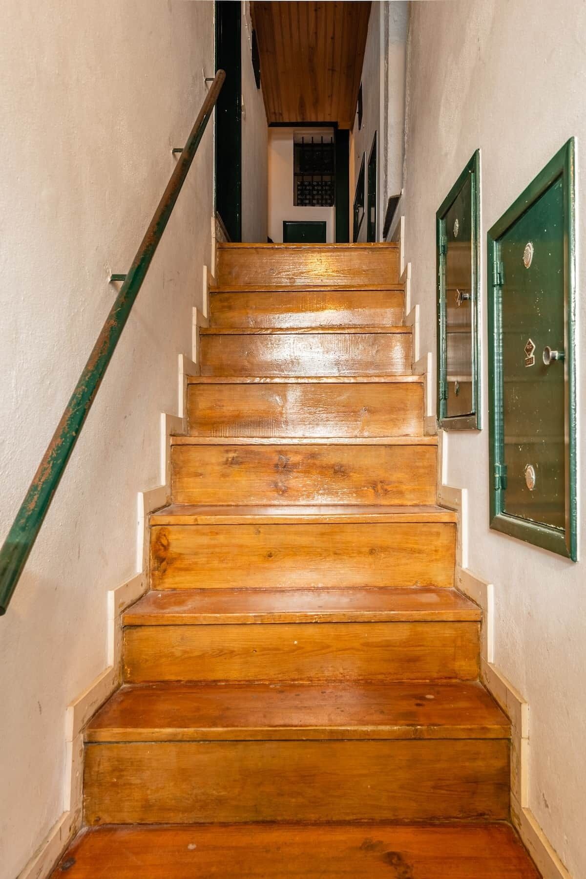 A wooden staircase with a handrail and green doors at the top.