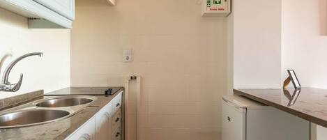 Una cocina compacta con dos lavamanos de acero inoxidable, un refrigerador blanco y un armario blanco con manija.