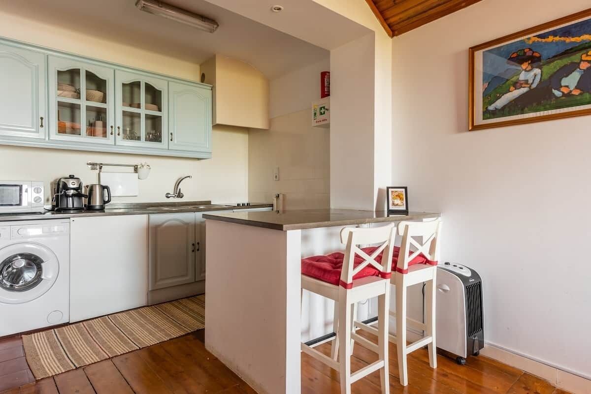 A compact kitchen with a washing machine, a coffee maker, and a small island with two chairs.