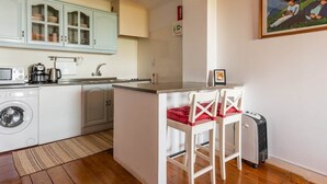 A compact kitchen with a washing machine, a coffee maker, and a small island with two chairs. - River View Studio Alfama (Lisbon)