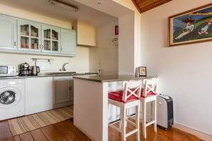 A compact kitchen with a washing machine, a coffee maker, and a small island with two chairs. - River View Studio Alfama (Lisbon)