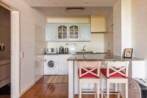 A compact kitchen with a washing machine, a microwave, and a sink. There are two chairs with red cushions at a small table. - River View Studio Alfama (Lisbon)