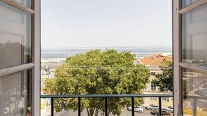 A view from a window with a balcony, overlooking a tree and a distant body of water. - River View Studio Alfama (Lisbon)