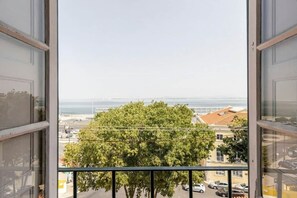 A view from a window with a balcony, overlooking a tree and a distant body of water. - River View Studio Alfama (Lisbon)