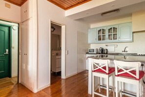 A kitchen with white cabinets, a microwave, and a coffee maker. There are two white bar stools with red cushions. - River View Studio Alfama (Lisbon)