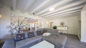 A modern living room with a grey sectional sofa, a white coffee table, and a large window with white flowers. - Villa Zenitude—Indoor Pool, Jacuzzi, and Sauna (Jezainville)