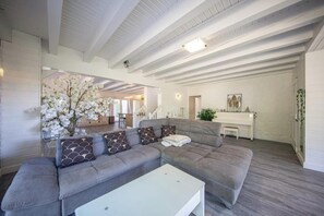 Ein modernes Wohnzimmer mit einem grauen Ecksofa, einem weißen Couchtisch und einem großen Fenster mit weißen Blumen.