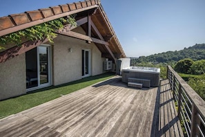Une terrasse en bois avec un jacuzzi, un espace patio couvert et une vue sur un paysage vallonné.