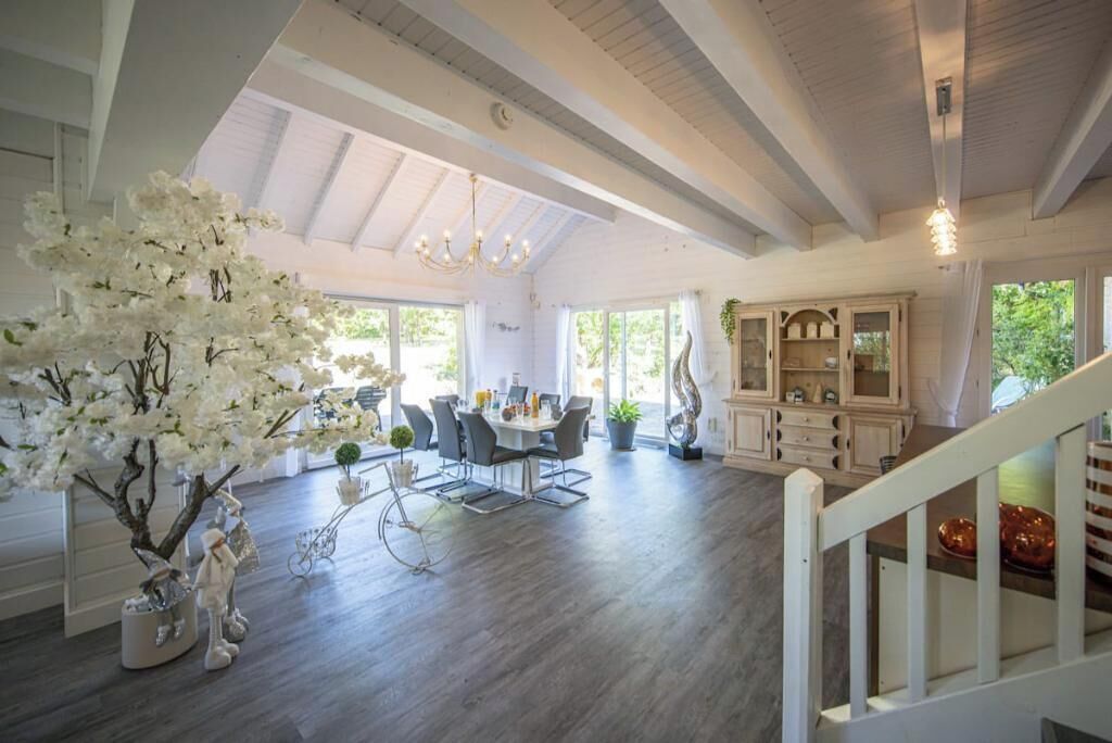 Amplia sala de estar con mesa de comedor, sillas y un gran árbol blanco. Se ve una escalera que sube a otro nivel.