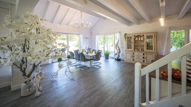 A spacious living area with a dining table, chairs, and a large white tree. There is a staircase leading to another level. - Villa Zenitude—Indoor Pool, Jacuzzi, and Sauna (Jezainville)