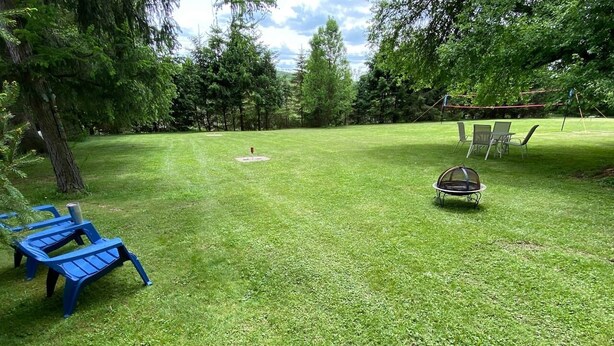 Un espacio al aire libre con césped, una mesa de picnic y sillas, una hamaca y una red de voleibol.