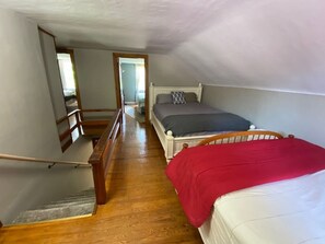 A bedroom with a wooden staircase, a bed with a red blanket, and a view of another room through an open door. - Rushford Lakeside Family Getaway (Houghton)