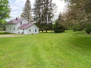 Uma casa de dois andares com telhado vermelho, rodeada por um gramado bem cuidado e árvores altas.