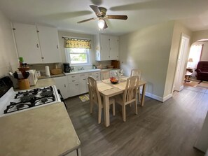 A kitchen with a gas stove, wooden cabinets, a dining table with chairs, and a ceiling fan. - Rushford Lakeside Family Getaway (Houghton)