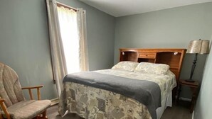 Un dormitorio con cama, una silla y una mesita de noche.