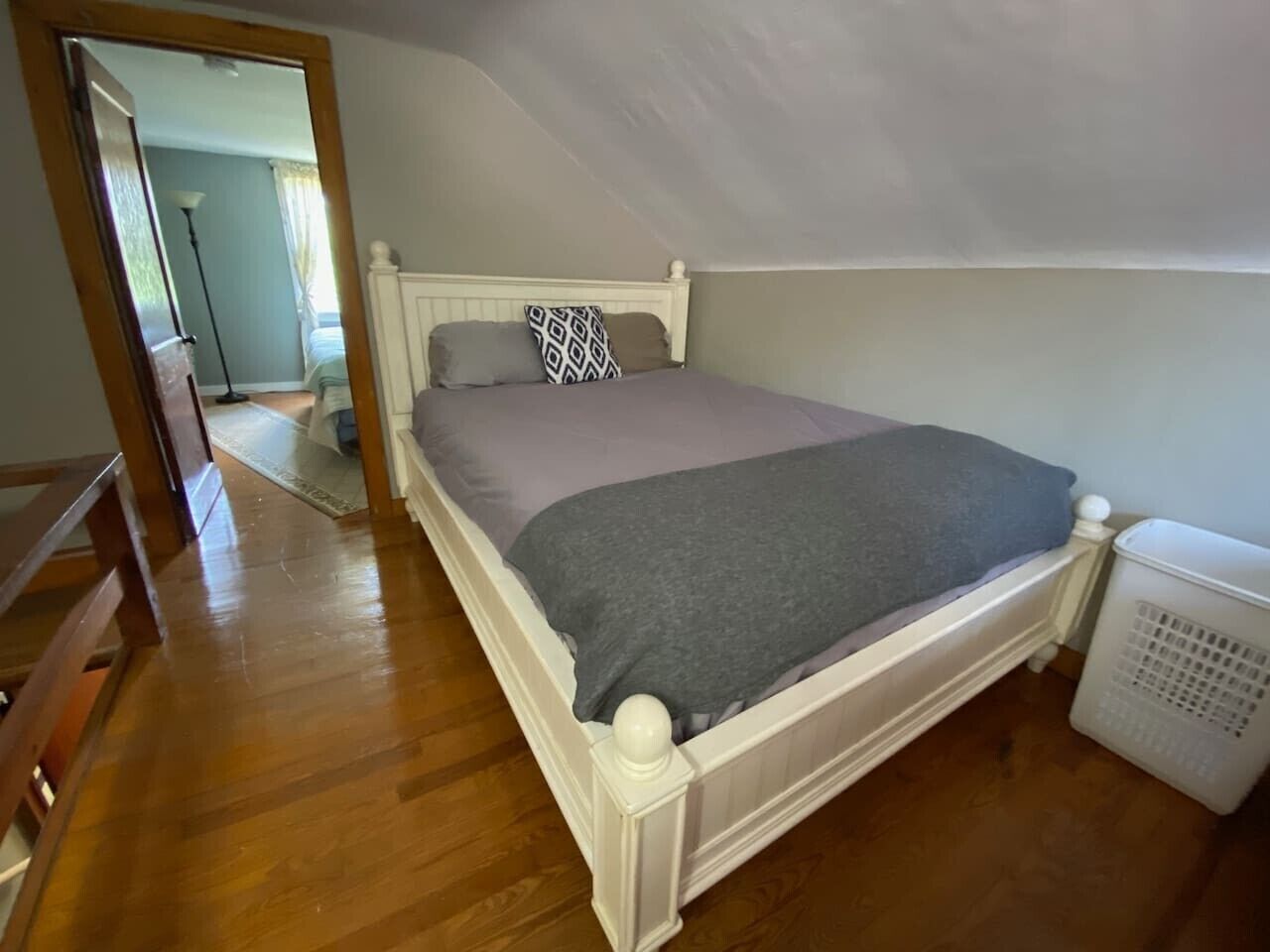 A bedroom with a wooden floor, a white bed with a grey blanket, and a white radiator.