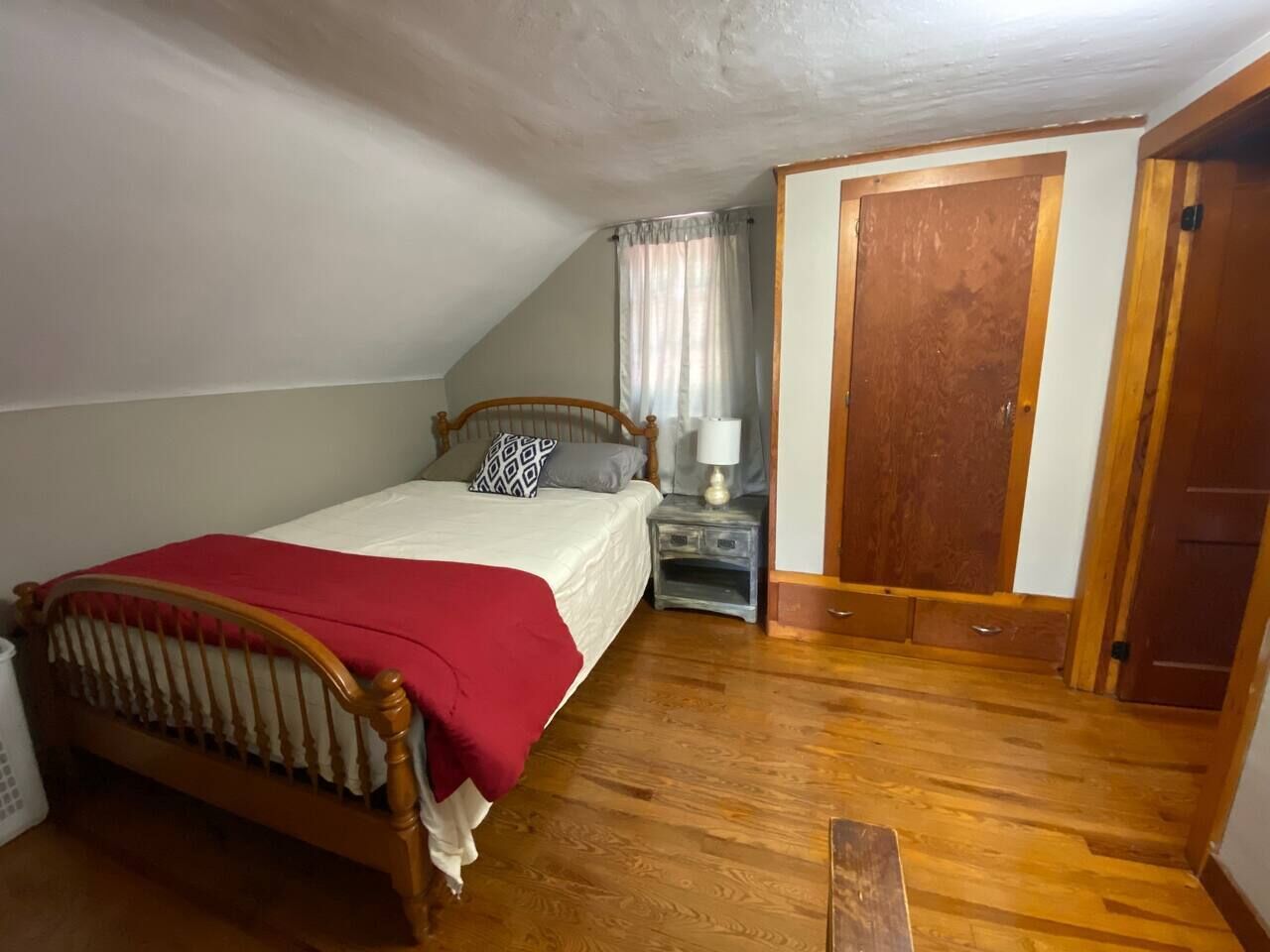 A bedroom with a wooden bed, a nightstand, a window with curtains, and a door.
