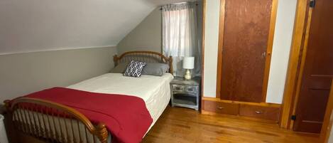 A bedroom with a wooden bed, a nightstand, a window with curtains, and a door.