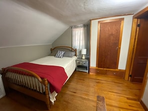 A bedroom with a wooden bed, a nightstand, a window with curtains, and a door. - Rushford Lakeside Family Getaway (Houghton)