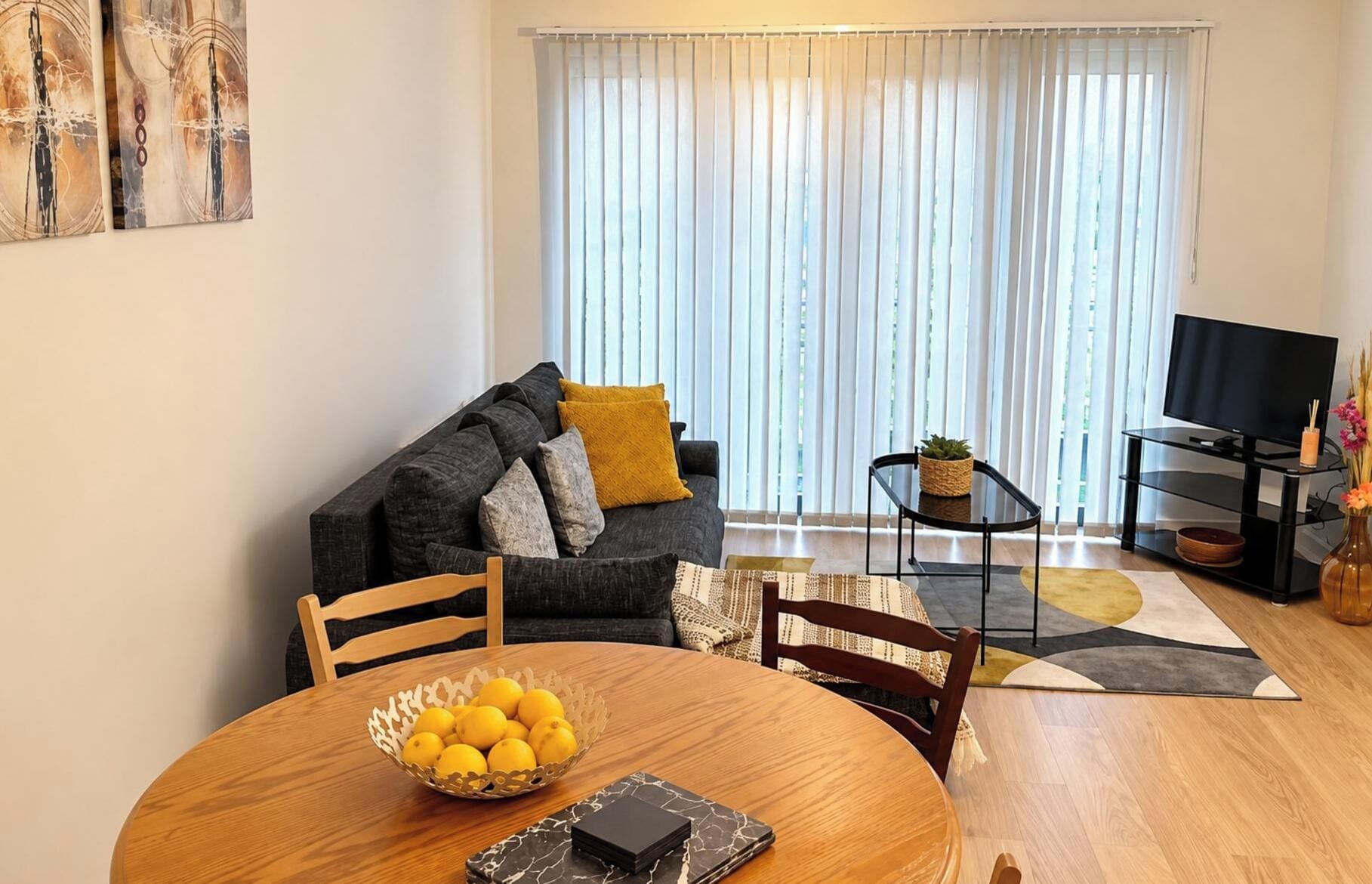 A living room with a sofa, a coffee table, a TV, and a dining table with a bowl of lemons.