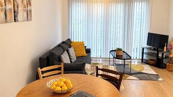 A living room with a sofa, a coffee table, a TV, and a dining table with a bowl of lemons.