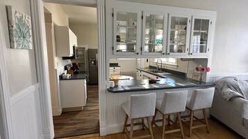 Une cuisine dotée d’un îlot central, de meubles blancs et d’un canapé gris dans l’espace de vie adjacent.