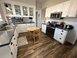 Une cuisine avec des meubles blancs, une table à manger en bois et un four encastré.