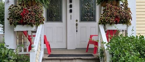 A two-story house with a front porch, a set of stairs leading to the front door, and two potted plants on either side of the door.