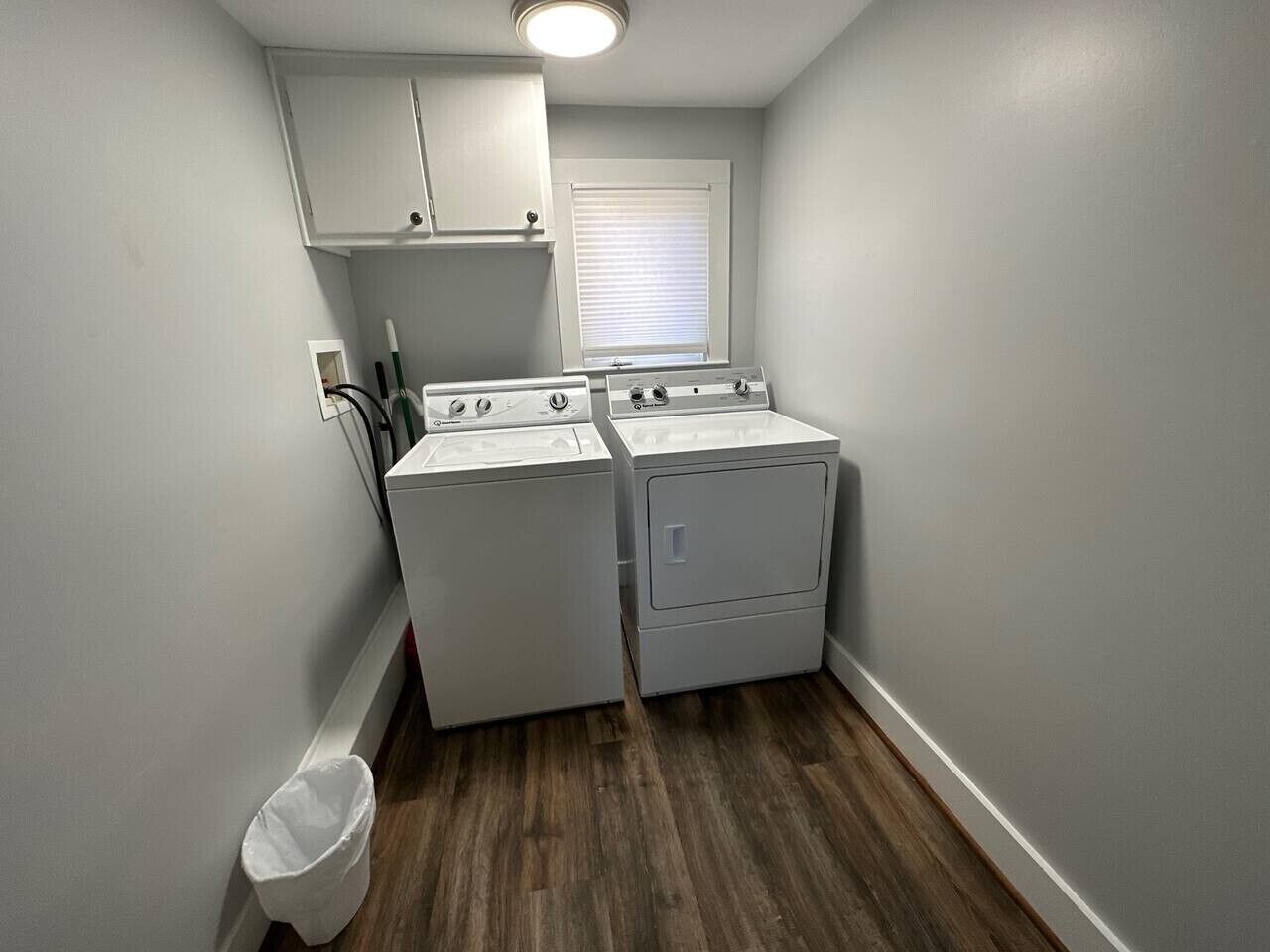 A laundry room with a washing machine, dryer, and a small trash bin.
