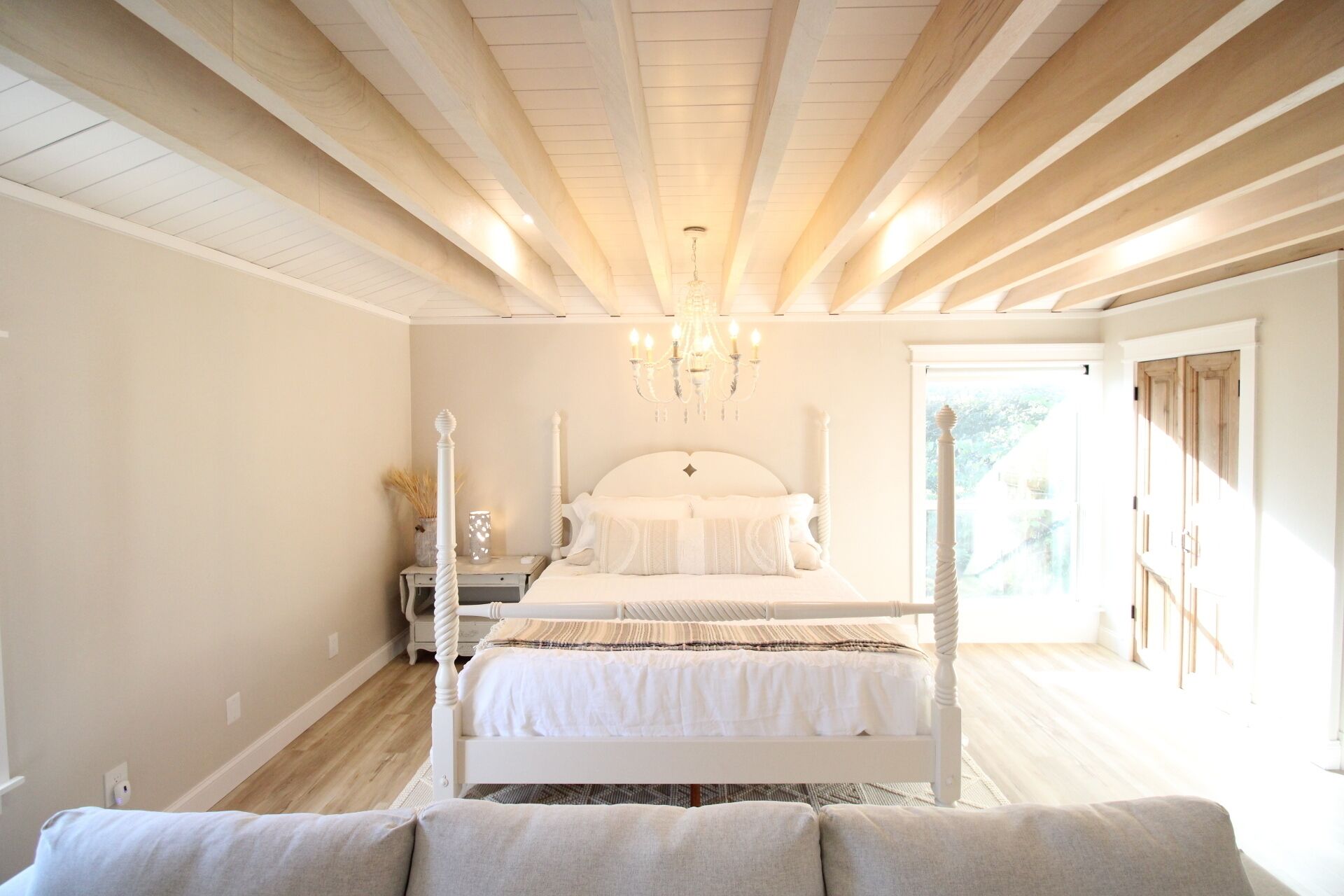 A bedroom with a four-poster bed, a chandelier, and a view of the outdoors.
