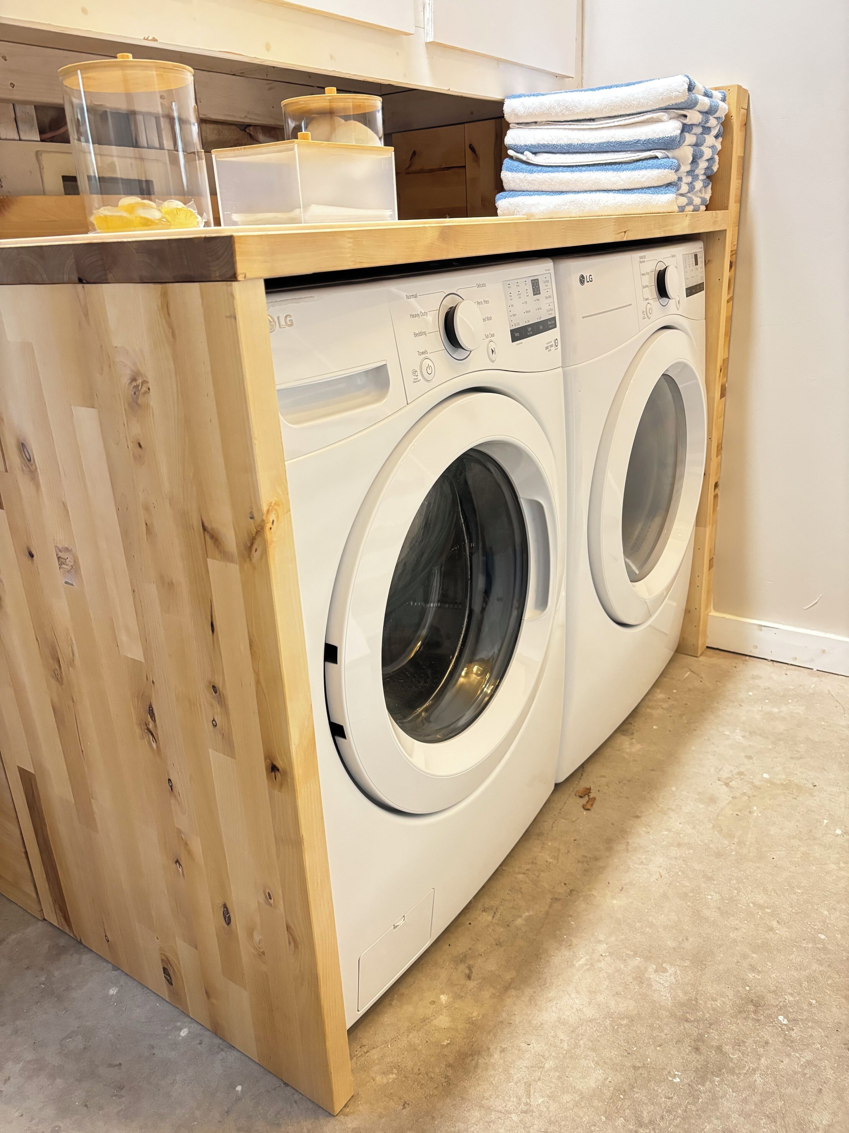 A compact laundry station with a washing machine and dryer, wooden cabinets, and a stack of towels.