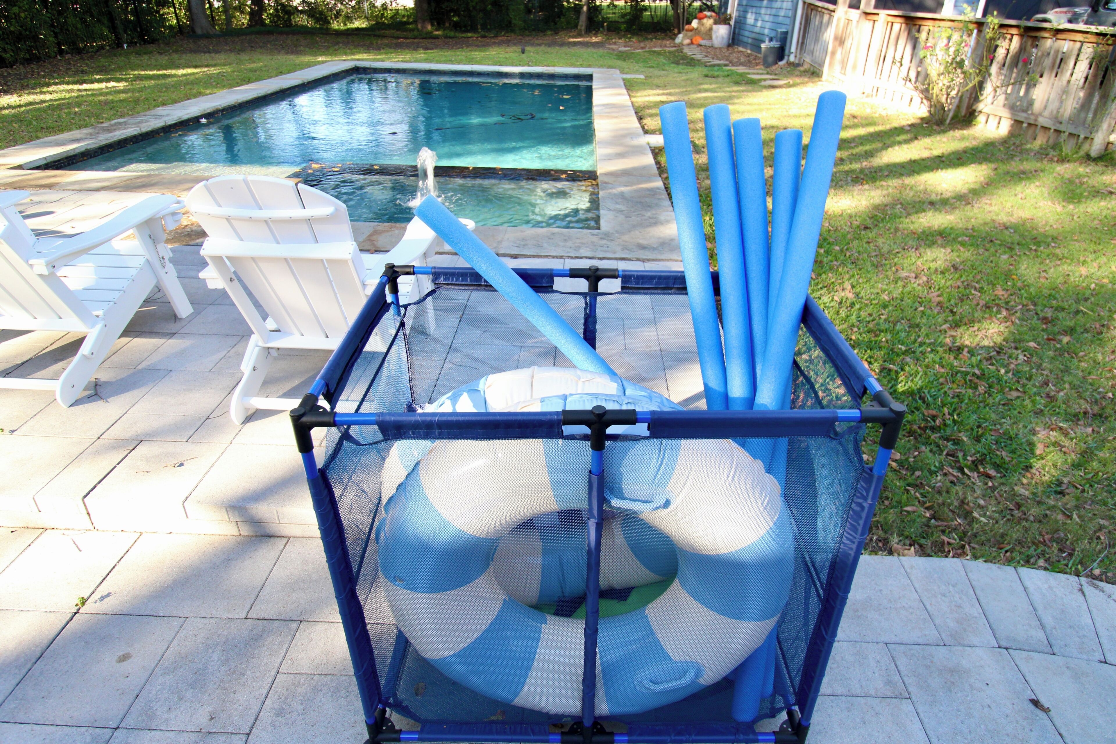 A poolside area with a pool, lounge chairs, and a storage box with blue pool noodles.