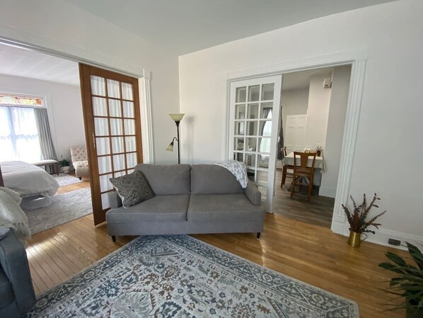 Una sala de estar con un sofá, un tapete estampado y un comedor con sillas y una mesa.