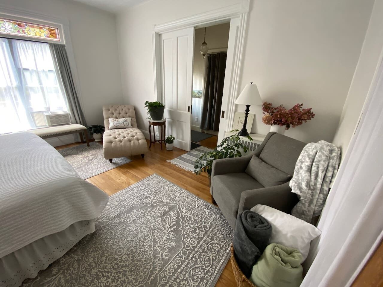 Une pièce comprenant un lit, un canapé gris, une chaise, une petite table avec une plante et une lampe.
