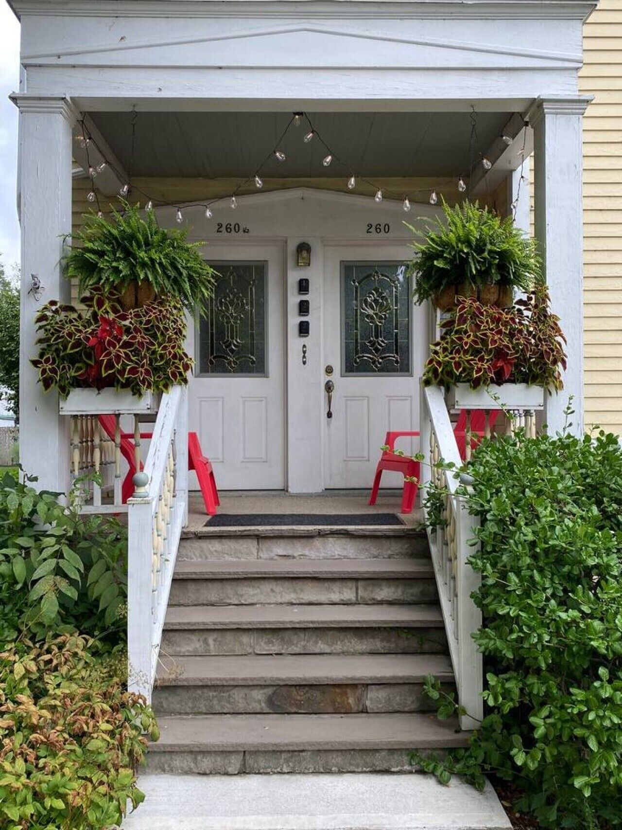A two-story house with a front porch, a set of stairs leading to the front door, and two potted plants on either side of the door.