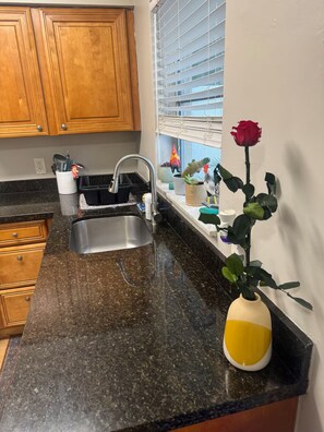 A kitchen with a granite countertop, a stainless steel sink, wooden cabinets, and a window with blinds. - 4-bedroom Pool house in serene Hollywood with cool AC breeze (Hollywood)