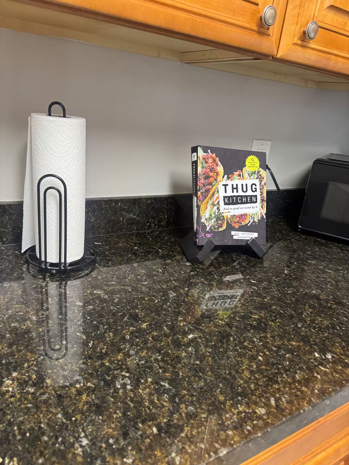 Een keukenblad met een keukenrolhouder, een magnetron en een kookboek getiteld 'Thug Kitchen' op een standaard.