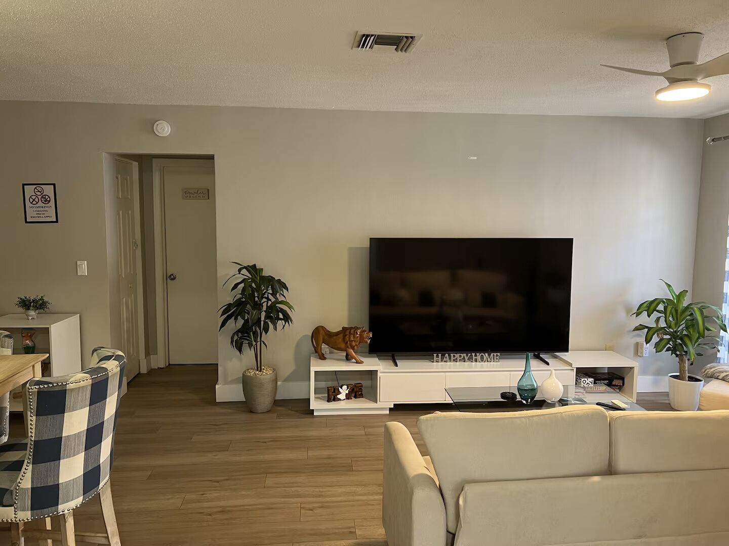 Uma sala de estar com televisão de tela plana, sofá, mesa de centro e ventilador de teto.