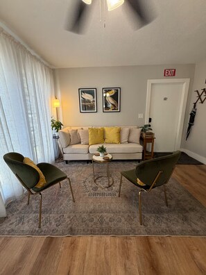 A living room with a sofa, two armchairs, a coffee table, and a rug. There are two framed pictures on the wall, a lamp, and an exit sign. - 4-bedroom Pool house in serene Hollywood with cool AC breeze (Hollywood)