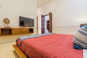 Ein Schlafzimmer mit einem Bett, einem Fernseher auf einem Holztisch, einer Tür zu einem Badezimmer und einem Regal mit Gegenständen.