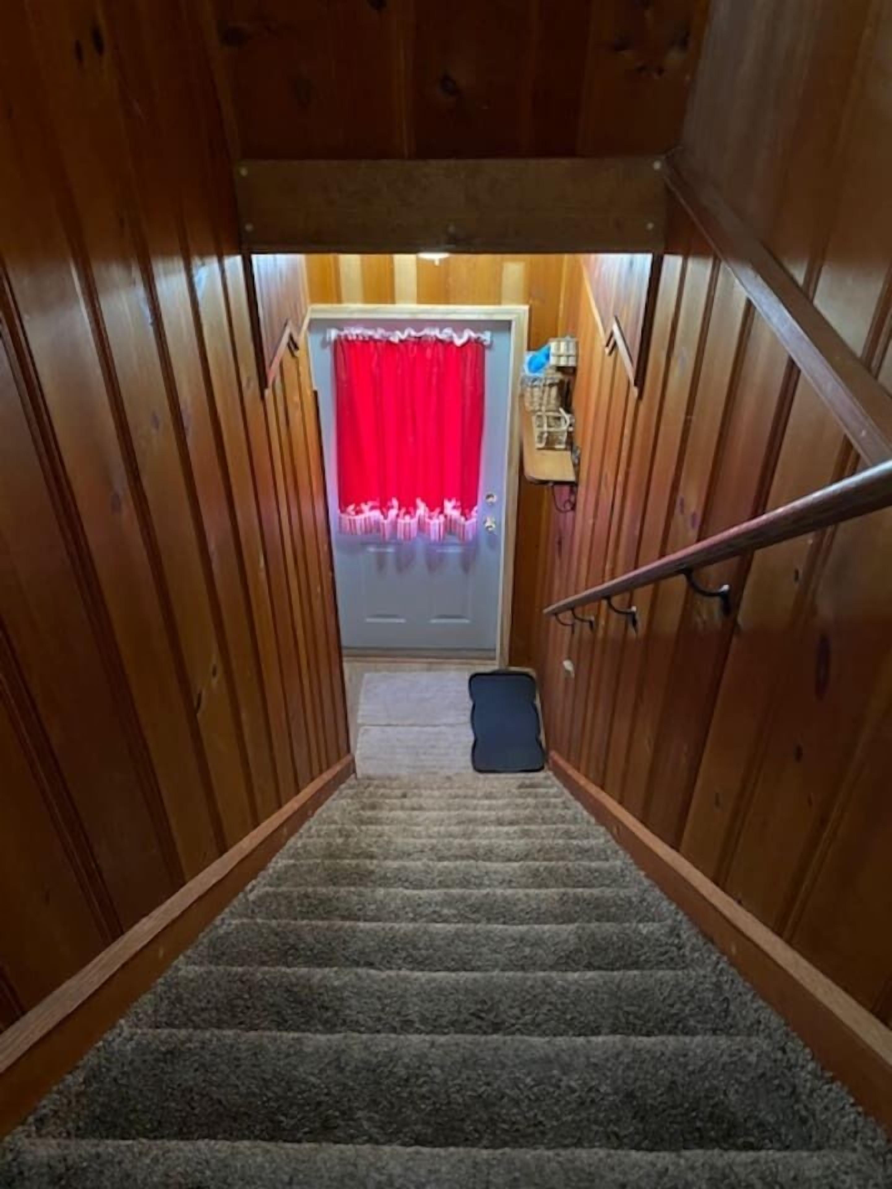 Un intérieur en bois avec un escalier recouvert de moquette menant à une porte ornée d’un rideau rouge.