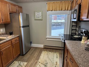 A kitchen with wooden cabinets, a stainless steel refrigerator, a window with a view of a snowy landscape, and a kitchen counter with a coffee maker.