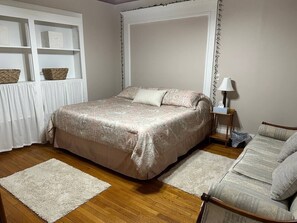 A bedroom with a bed, a nightstand, a lamp, and a sofa.