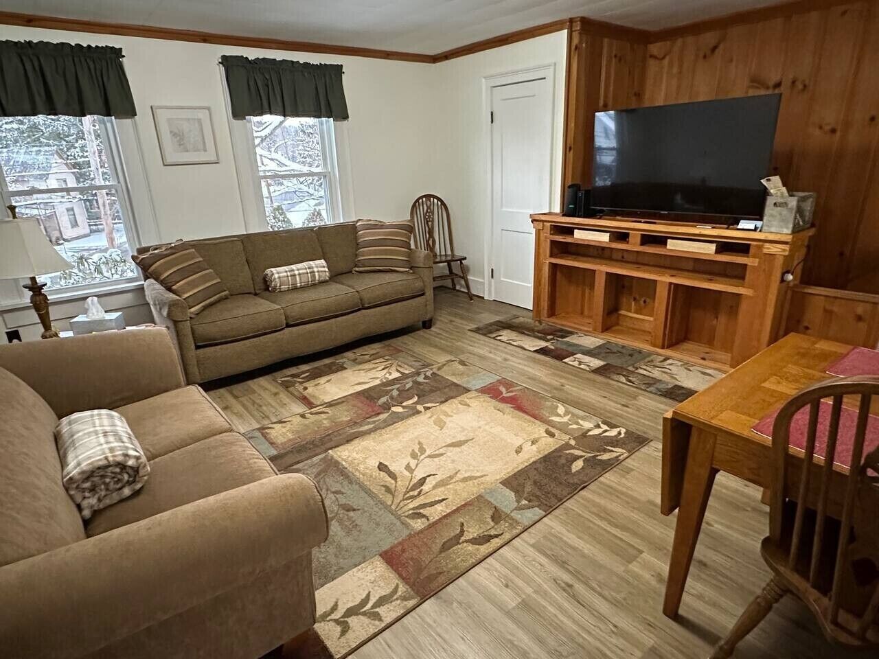 A living room with a sofa, a television on a wooden stand, a dining table, and a patterned rug.