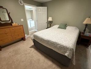 A bedroom with a bed, dresser, two bedside lamps, and a door leading to another room.